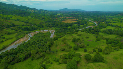 AERIAL: Slow river meanders past meadows and fields through a tropical landscape