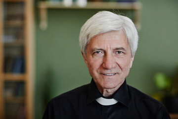 Close up portrait of white haired senior priest smiling at camera in office setting, copy space