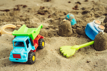 Fototapeta na wymiar children's beach toys made of plastic on the sand near the sea trucks watering can rake