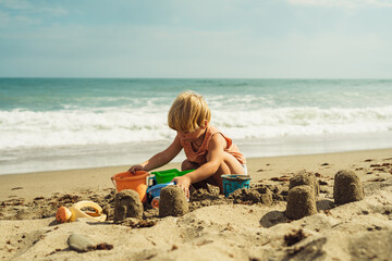boy 3 years old blond plays on the seashore in the sand with plastic toys against the background of the sea