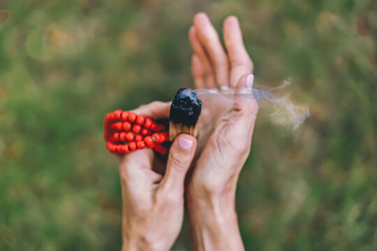 Top angle view of a palo santo or a holy sacred tree stick, burning with aroma smoke held by woman's hands over nature background
