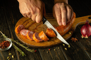 Sliced meat sausage. Knife in the chef hand for cutting sausage on a cutting kitchen board