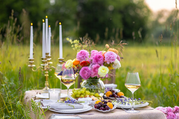 Elegant fancy wedding table decor with bright ranunculi flowers in a vase outdoors, chandelier,...