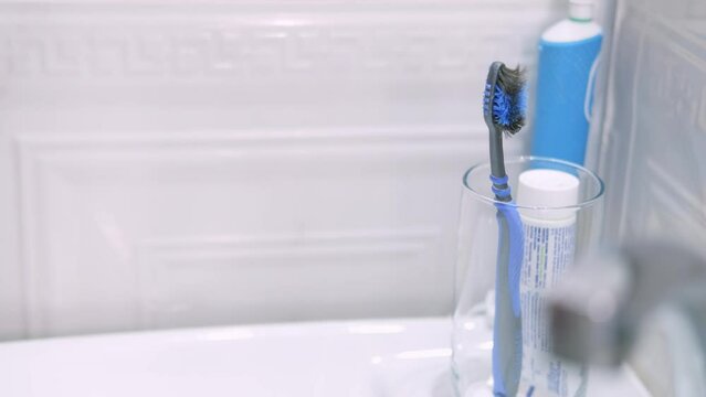 kids hand takes toothbrush from glass in bathroom at home, Health care, dental hygiene, bad old brushes