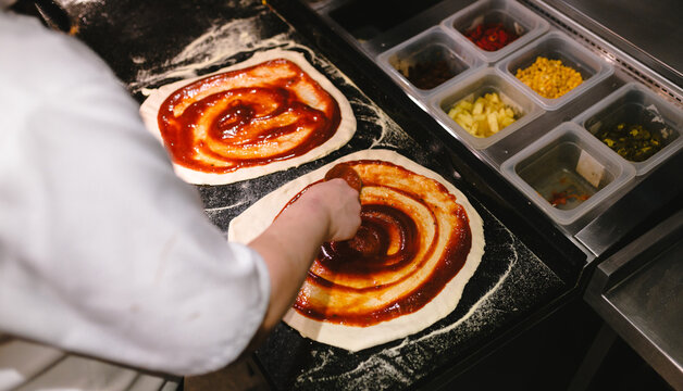 Chef preparing a pizza spreading tomato sauce