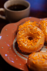 Orange glazed donuts with orange sugar sprinkles and coffee.