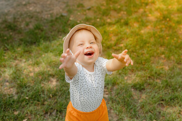 A young boy in an adorable hat beams with happiness as he stretches his arms toward his parent,...