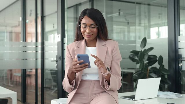 Busy Young Professional African American Business Woman Executive Finance Manager Holding Cellphone Using Mobile Looking At Cell Phone Technology In Office Working On Smartphone.