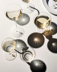 Aerial view of series of champagne glasses with shadows and reflections on white surface