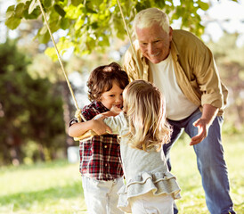 Young boy and girl using a swing in the park with their grandfather
