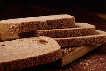 Sliced brown bread covered with bran on a wooden board on the dark wooden table. Macro shot.
