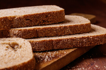 Sliced brown bread covered with bran on a wooden board on the dark wooden table. Macro shot.