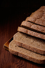 Sliced brown bread covered with bran on a wooden board on the dark wooden table.