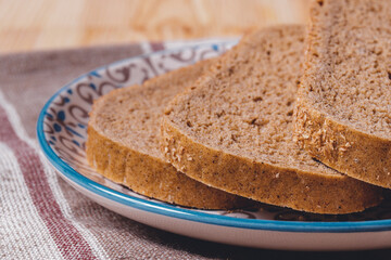 Sliced brown bread covered with bran in a plate on a tablecloth.