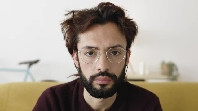 Portrait of serious mid adult bearded man looking at camera sitting on couch at home. 