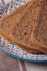 Sliced brown bread covered with bran in a plate on a tablecloth.
