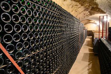 Fototapeta premium Walking in deep undergrounds caves with bottles on wooden racks, making champagne sparkling wine from chardonnay and pinor noir grapes in Epernay, Champagne, France