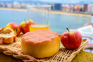 Asturias food and drink, smoked cow cheese from Pria served outdoor with glass of natural apple cider and view on San Lorenzo beach in Gijon