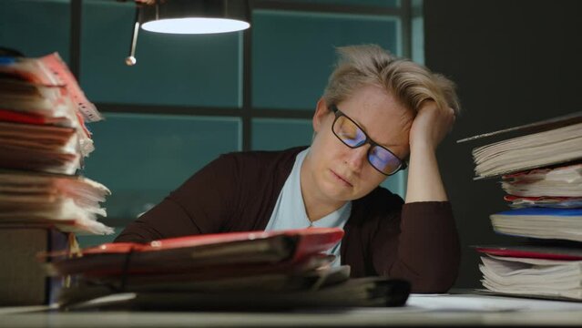 Sleeping woman at work in office late at night sitting at desk. Overworked female employee fell asleep at workplace from fatigue during overtime.