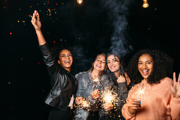 Four young females hanging out at night. Women celebrate with confetti and sparklers.