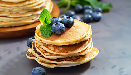 Pancakes with blueberries and mint leaf on top. Pile of small homemade pancakes with forest fruits. Heap of flat thin cake in background.