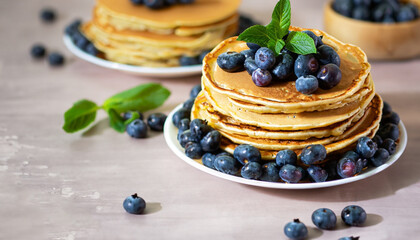 Pancakes with blueberries and mint leaf on top. Pile of small homemade pancakes with forest fruits. Heap of flat thin cake in background.