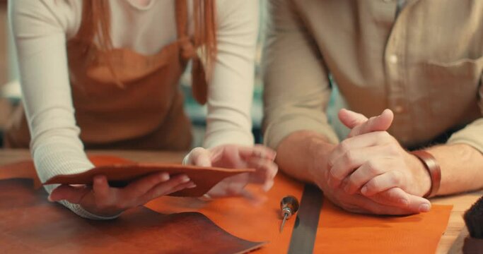 Professional male and female crafter choosing brown orange leather for making leather items Slow motion red-haired woman handsome man talking discussing future leather goods