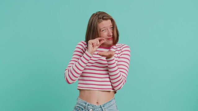 Need some more, please give me, help. Woman showing a little bit gesture with sceptic smile, showing minimum sign measuring small size. Pretty girl in crop top isolated alone on blue studio background