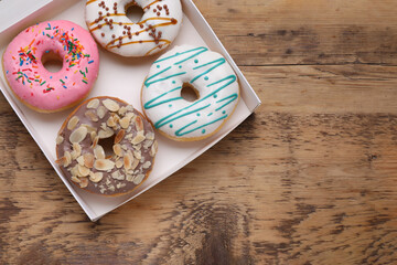 Box with different tasty glazed donuts on wooden table, top view. Space for text
