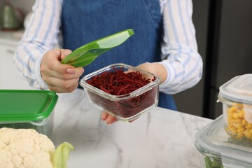 Woman holding open container with cut fresh red beets at white marble table in kitchen, closeup....