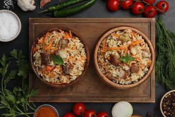 Delicious pilaf in bowls and products on black table, flat lay