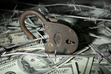 Lock with barbed wire on dollar banknotes, closeup. Sanctions concept