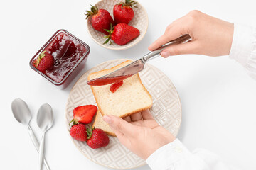 Woman preparing tasty toasts with sweet strawberry jam on light background