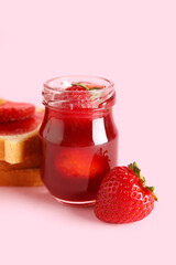 Jar of sweet strawberry jam on pink background