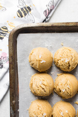Scoops of vanilla cookie dough on a parchment lined cookie sheet, plain vanilla cookie dough about to be baked