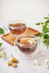 Glass cups of tea, sugar and beautiful jasmine flowers on light background