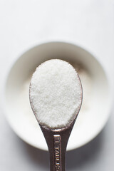A tablespoon of white sugar, top view of granulated sugar in a rose gold measuring spoon