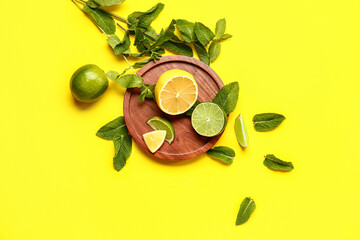 Wooden plate with lime, lemon and fresh mint leaves on yellow background