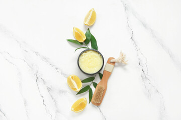 Bowl of lemon body scrub and massage brush on grunge white background
