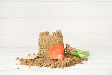 Castle made of sand with seashells and shovel on white wooden background