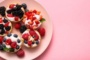 Plate of tasty tartlets with whipped cream and berries on pink background