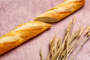 Sliced baguette and wheat ears on pink table