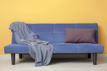 Blue sofa with cozy blanket and cushion near orange wall