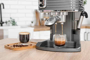 Modern coffee machine with glasses of hot espresso on table in kitchen