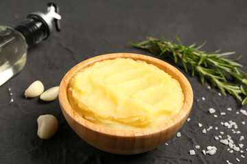 Wooden bowl of tasty mashed potatoes with rosemary and garlic on black background