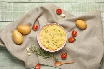 Bowl of tasty mashed potatoes with rosemary, tomatoes and garlic on green wooden background