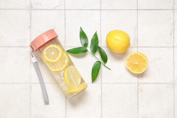 Sports bottle of infused water with lemon and leaves on white tile background