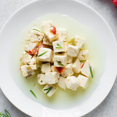 Top view of marinated feta cheese cubes on white plate. Cheese cubes marinating in herbed oil, flat lay of feta cheese in olive oil on plate