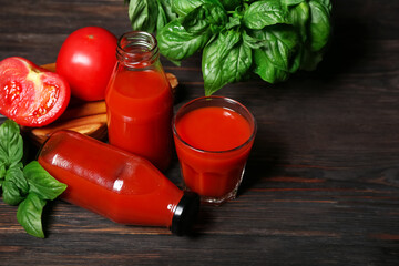 Glass and bottles of tasty tomato juice on black wooden background