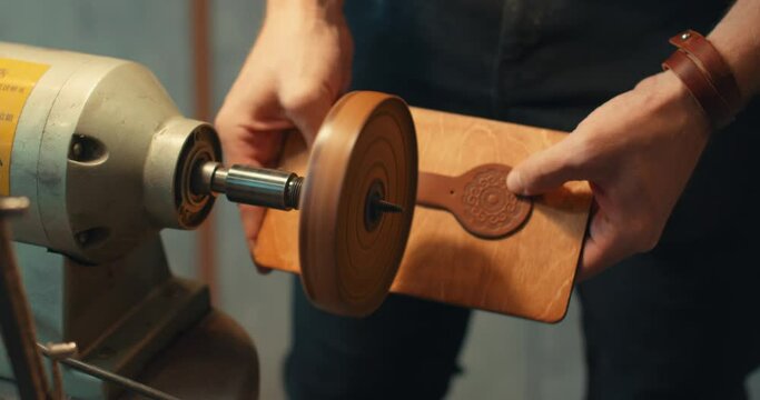 A craftsman is using an electric burnisher machine while sewing handmade wallet, accessories, items Slow motion. process of sewing handmade bag, wallet, purse